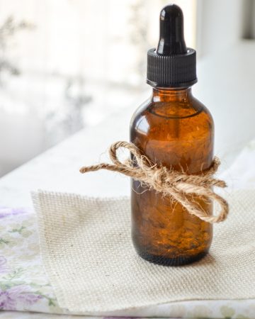 A bottle of facial serum with a piece of twine wrapped around the bottle, resting on several layers of fabric.