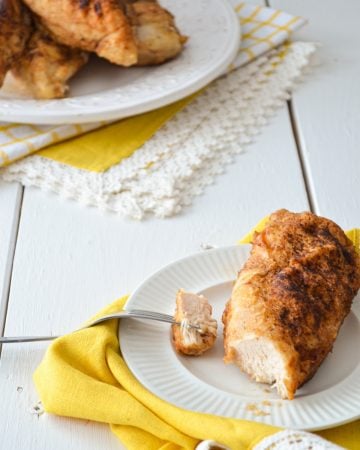 A piece of baked chicken on a white plate, resting on a yellow napkin.
