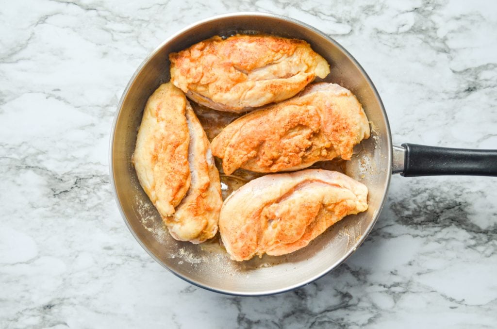 Chicken breasts cooked in a skillet with butter.