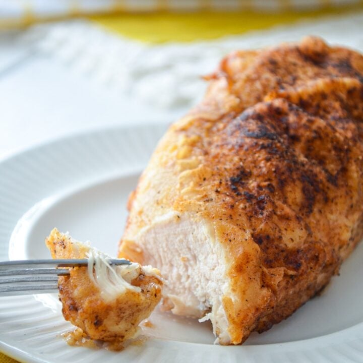 A juicy baked chicken breast on a plate, a fork with a small piece of the chicken.