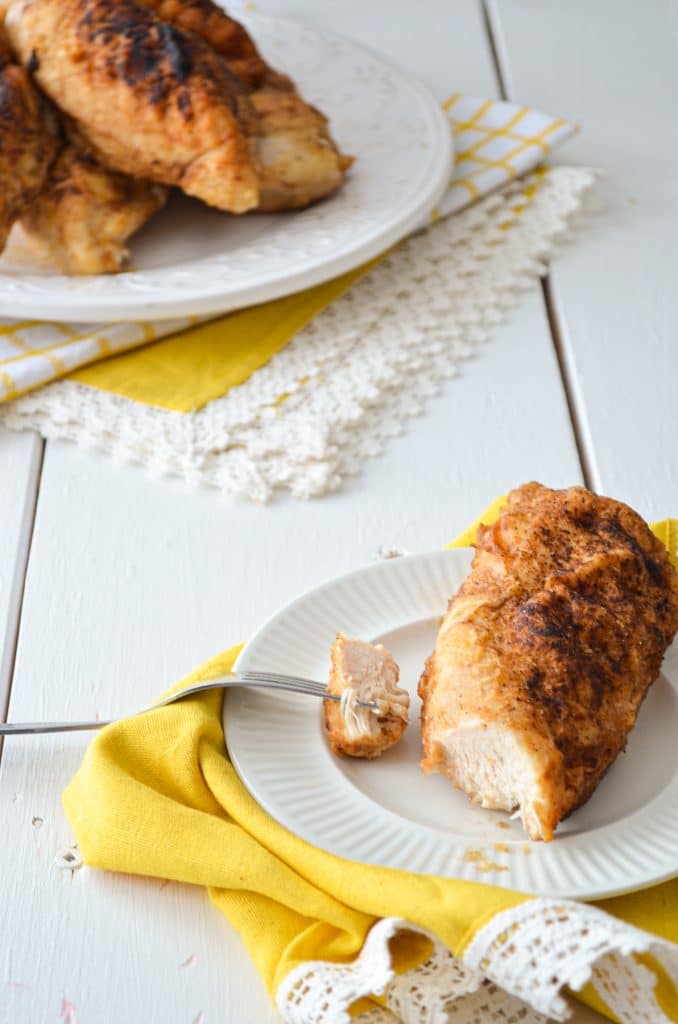 A small plate with a chicken breast on it. A larger plate in the background, filled with chicken breasts.