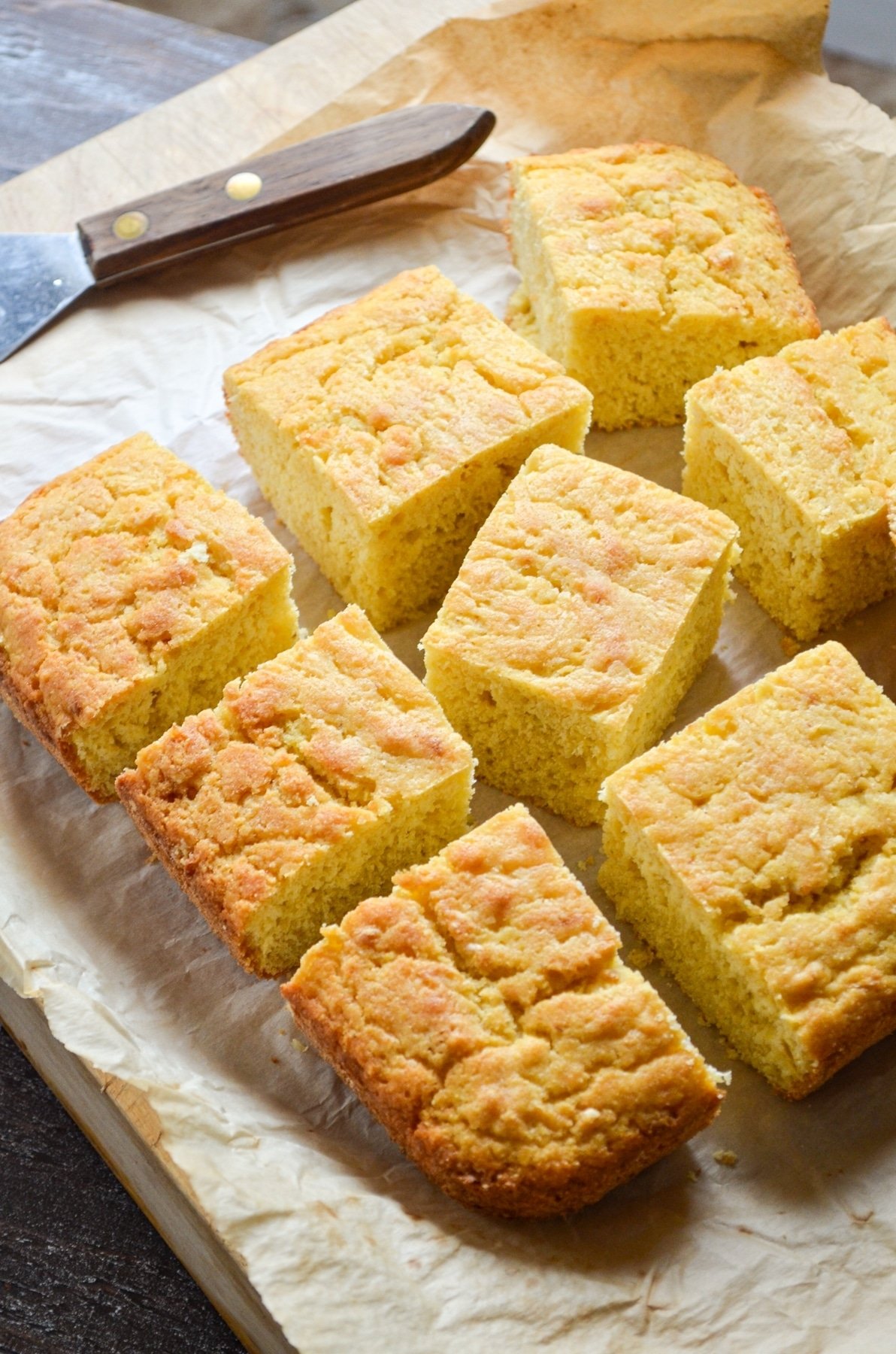 Cornbread on a parchment lined cutting board, cut into 9 pieces.