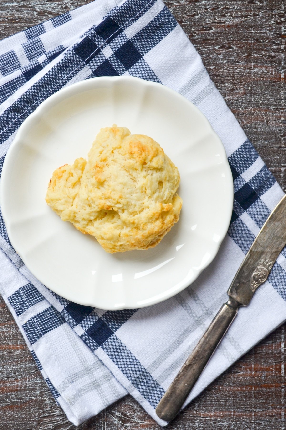 A sourdough discard drop biscuit on a white plate with a blue striped napkin.