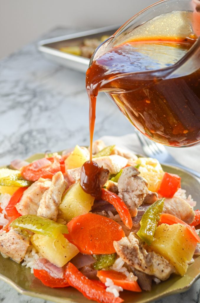 Sweet and sour sauce being poured on a dish of chicken and vegetables.