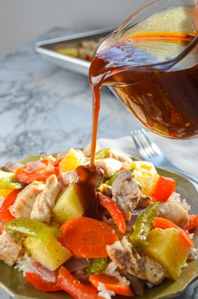 Sweet and sour sauce being poured on a dish of chicken and vegetables.