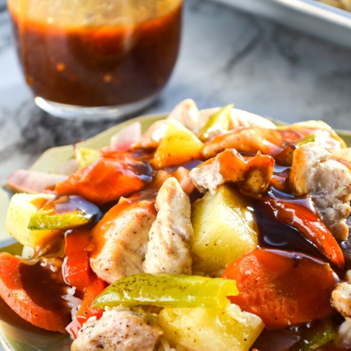 A plate of sweet and sour chicken with a small cruet of sweet and sour sauce in the background.