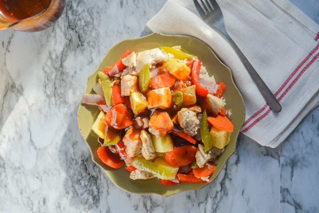 A plate of sweet and sour chicken with a fork to the right.