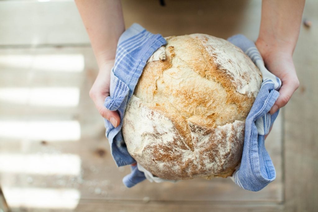 A loaf of bread, being held with a blue dishtowel.