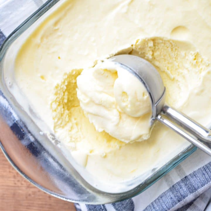 A scoop of orange creamsicle ice cream being taken out of a glass loaf pan.