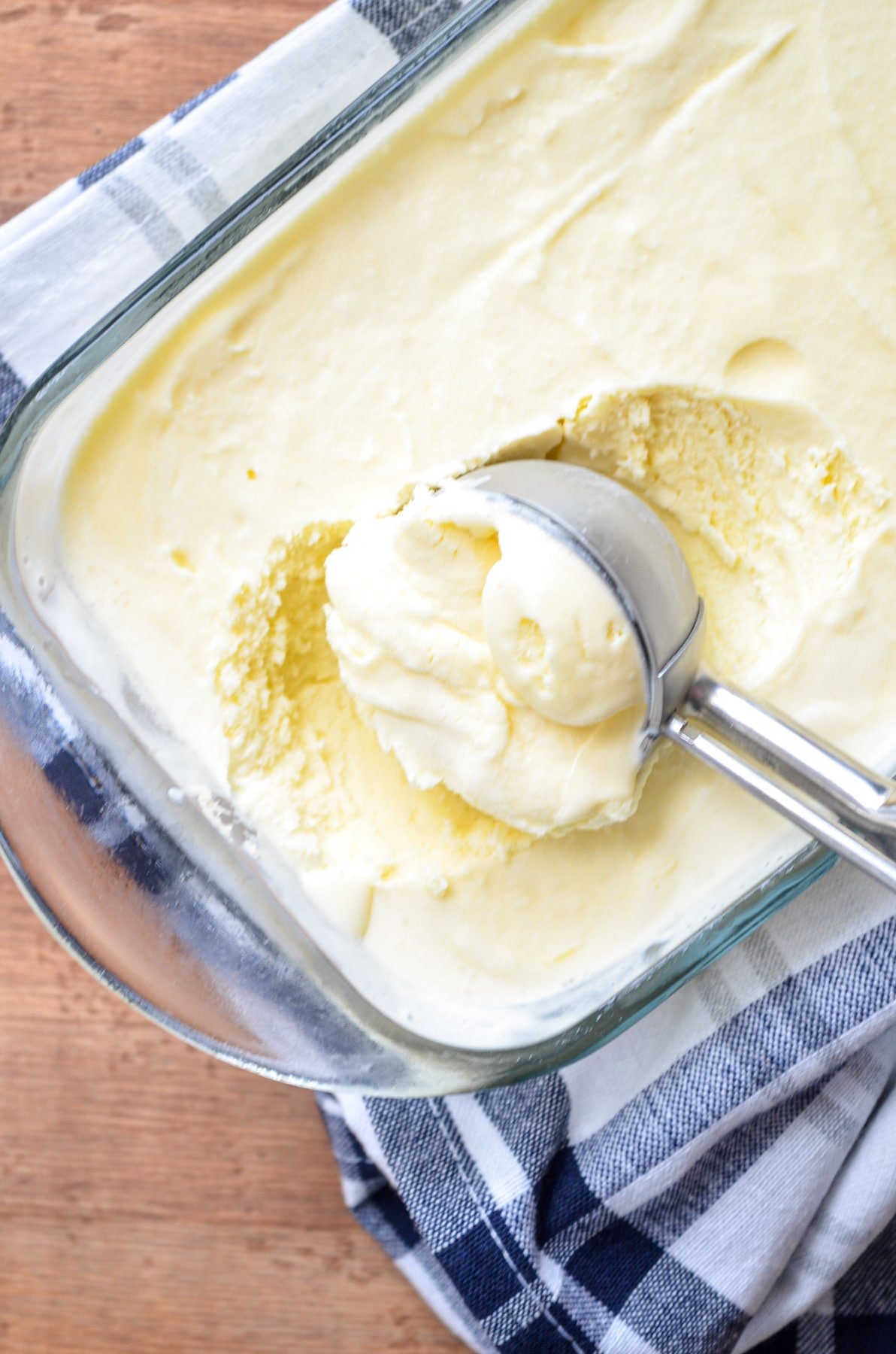 A scoop of orange creamsicle ice cream being taken out of a glass loaf pan.