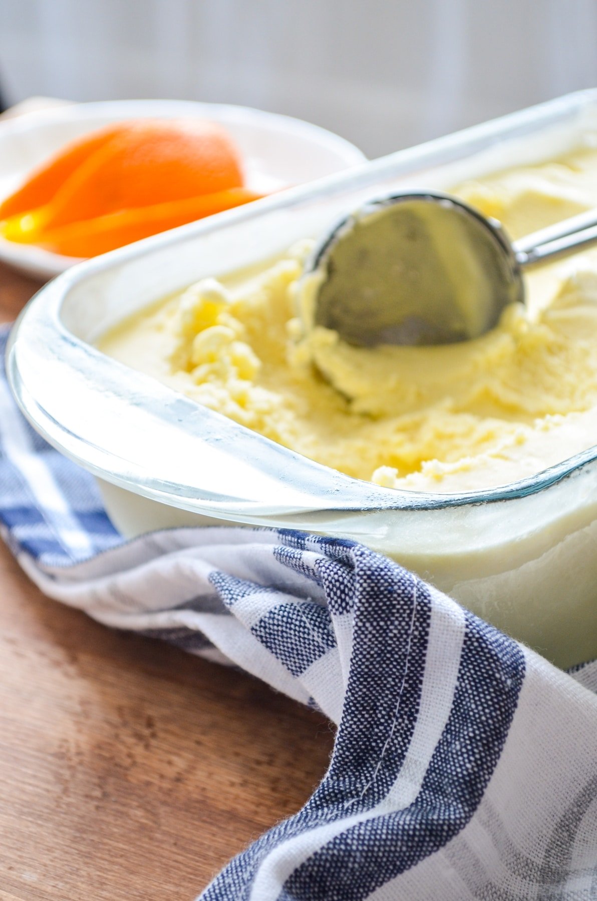 A loaf pan of orange creamsicle ice cream, an ice cream scoop inside.