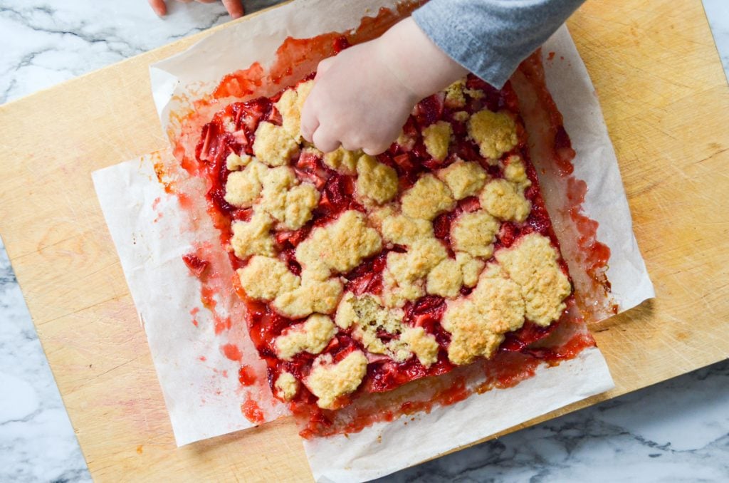 A toddler's hand reaching in and grabbing some strawberry crumb bar topping.