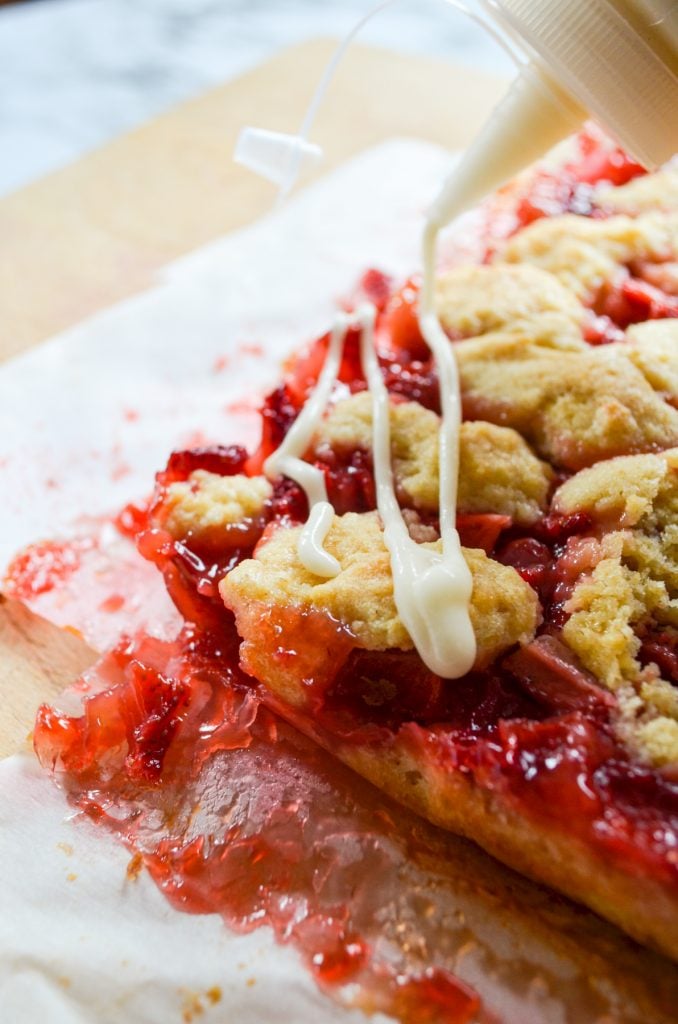 A strawberry crumb bar being drizzled with icing.