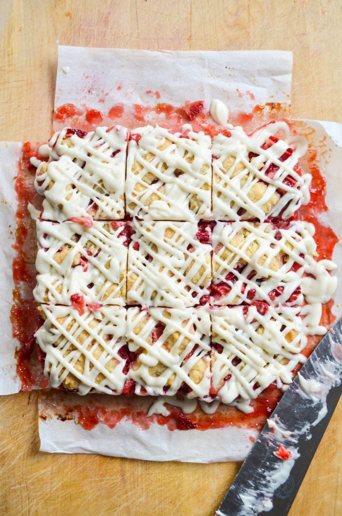 9 strawberry crumb bars with a knife, on a wooden cutting board.