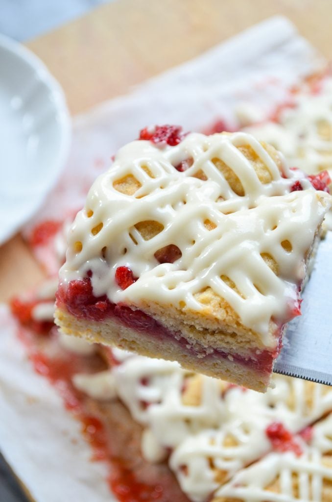 A strawberry crumb bar being lifted off a piece of parchment paper.