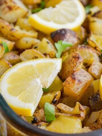 A pan of lemon garlic roasted potatoes, with lemon wedges on top.