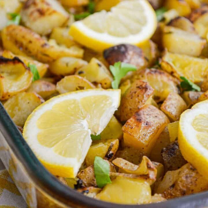 A pan of lemon garlic roasted potatoes, with lemon wedges on top.