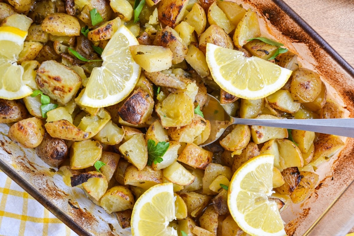 A baking dish full of roasted potatoes, garnished with lemon.