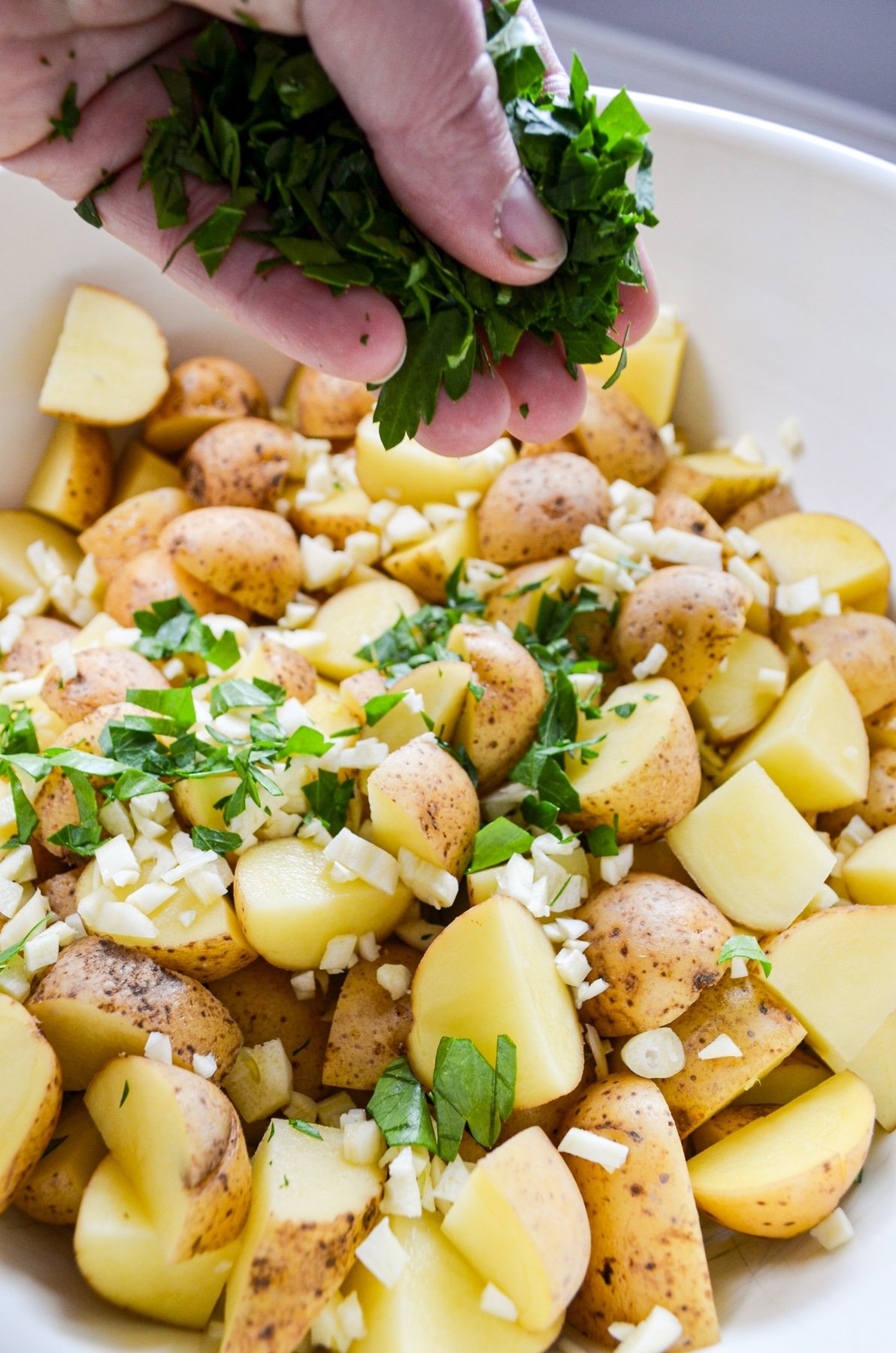 Sprinkling fresh parsley over a pan of roasted vegetables.