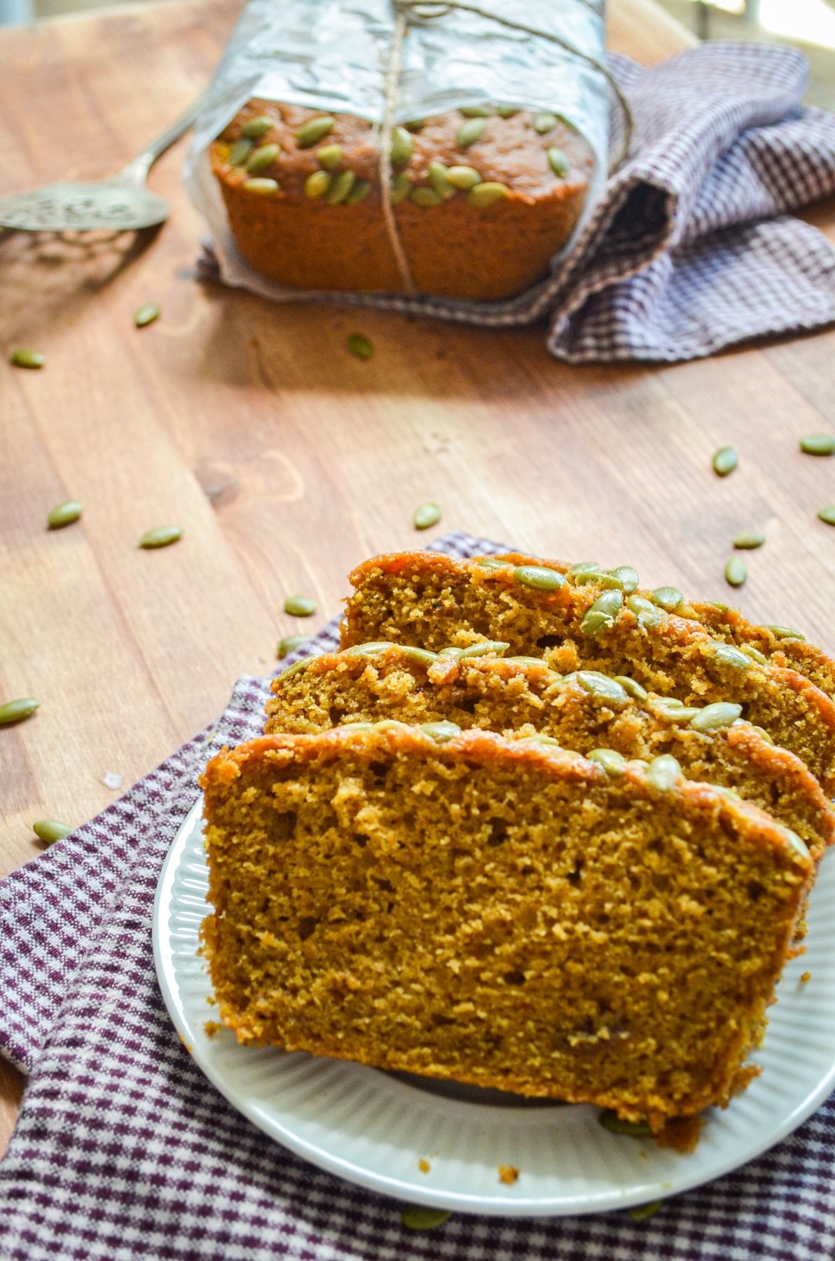 Several slices of pumpkin bread, with the full wrapped loaf in the background.