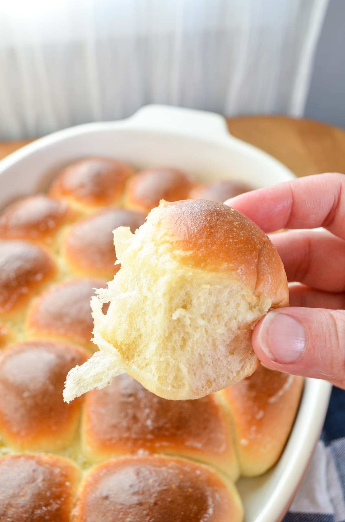 A hand holding a dinner roll from a large baking dish.