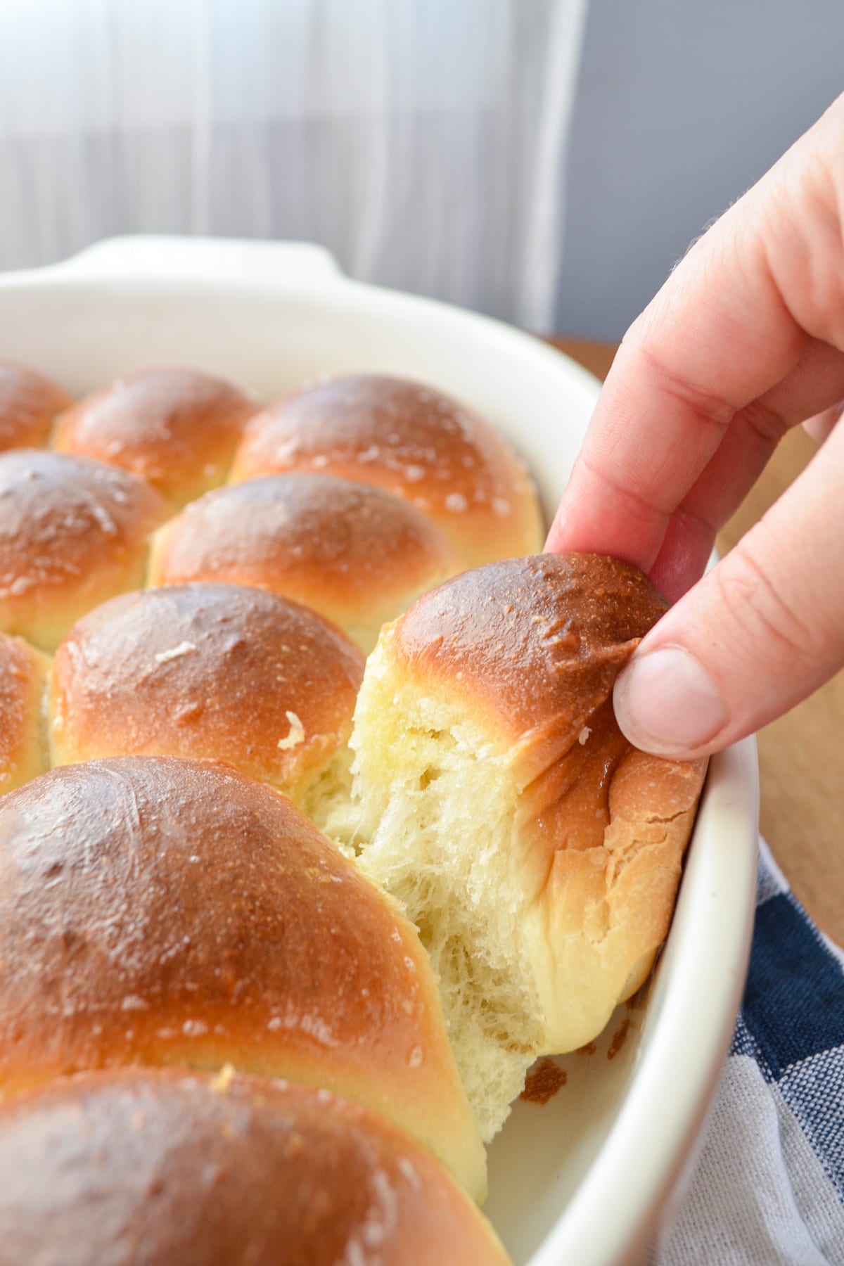 A soft and fluffy snowflake roll being pulled from a baking dish.