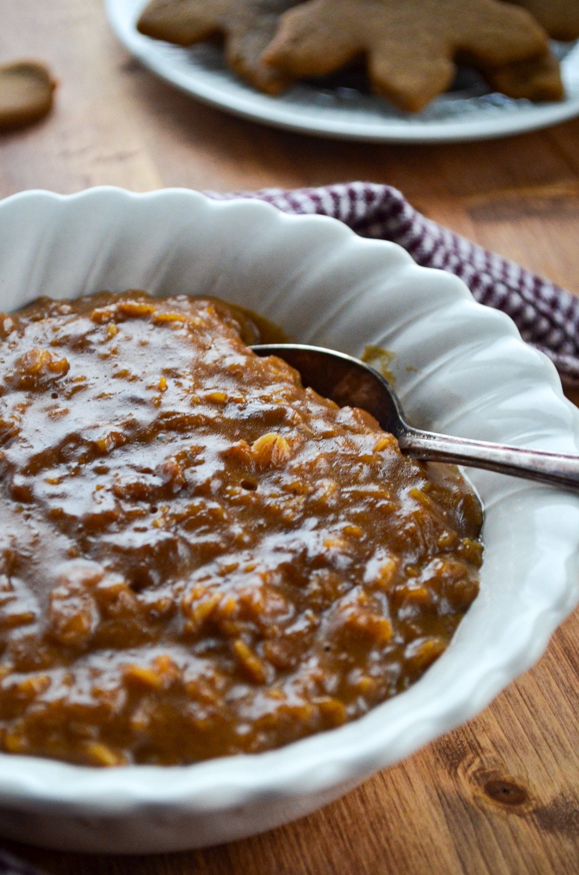 A bowl of gingerbread oatmeal, with cookies in the background.