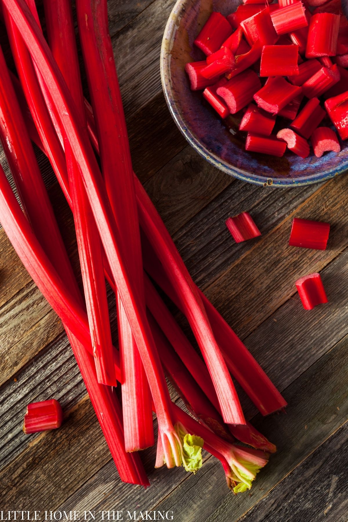 Rhubarb stems on a wood surface, with a bowl of chopped rhubarb on the side.