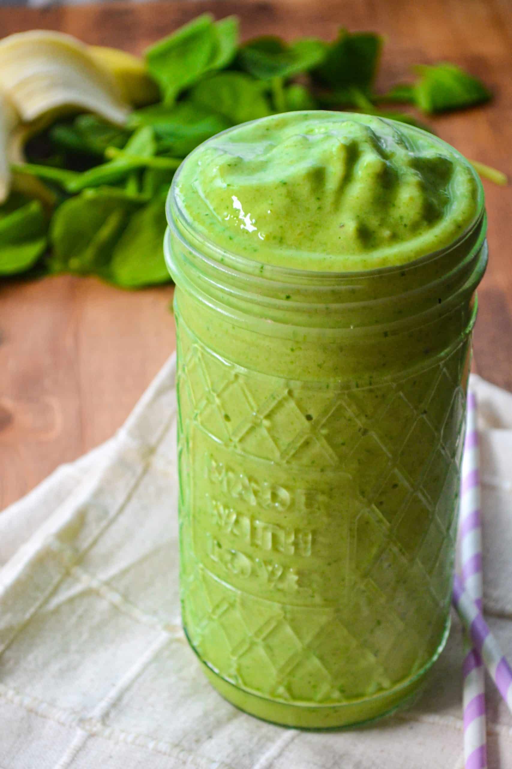 A large glass jar of green smoothie, with a purple straw for drinking.