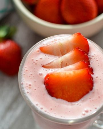 A glass of strawberry smoothie, garnished with fresh strawberry slices