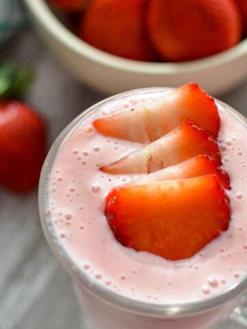 A glass of strawberry smoothie, garnished with fresh strawberry slices