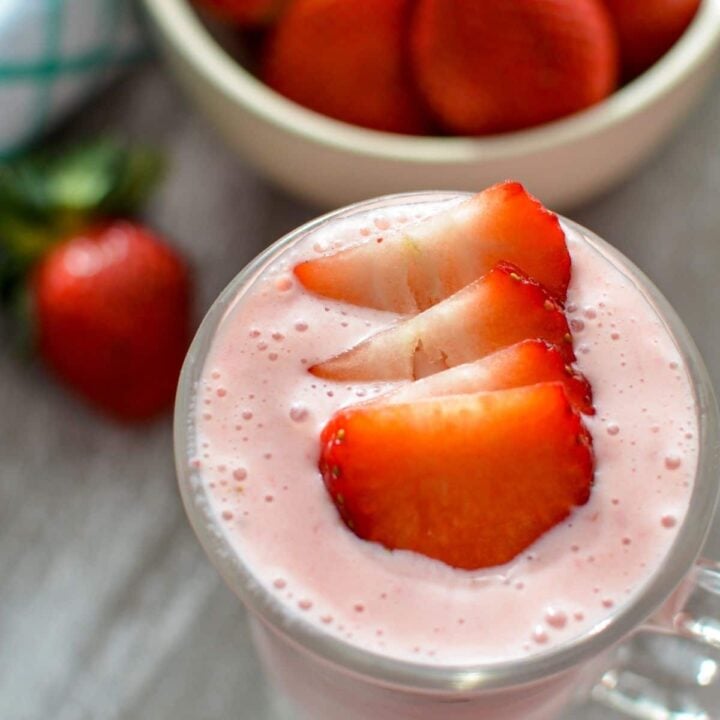 A glass of strawberry smoothie, garnished with fresh strawberry slices