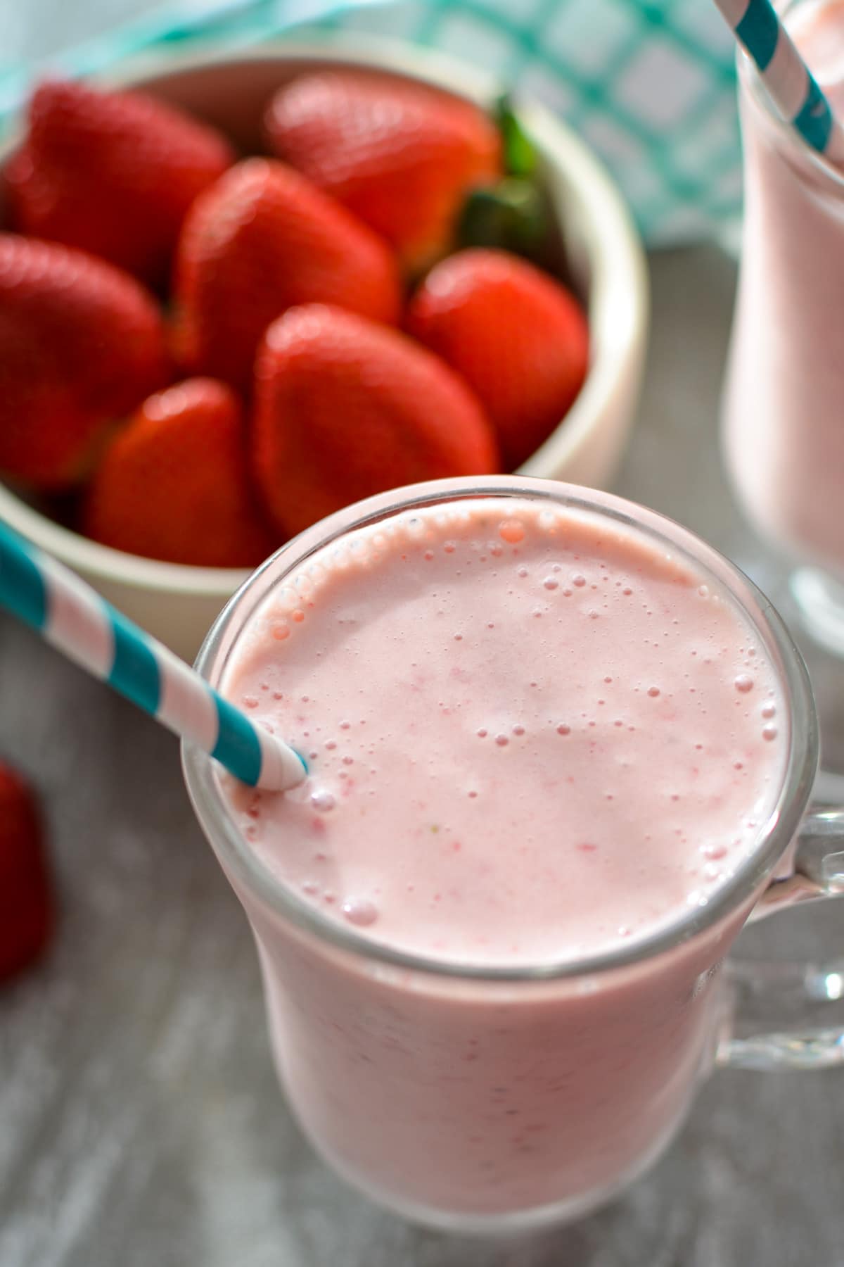 A glass of strawberry kefir smoothie, with a bowl of fresh berries in the background.