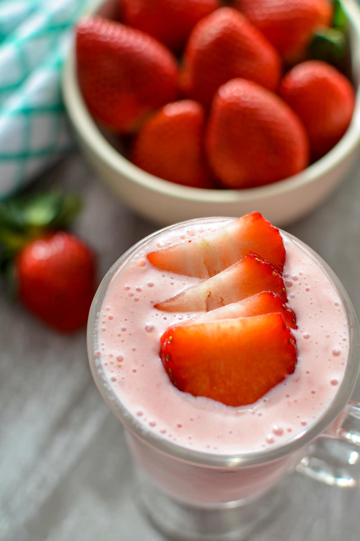 A strawberry smoothie with a bowl of fresh strawberries in the background.