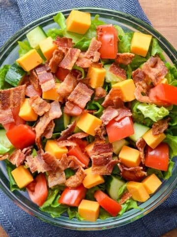 A bowl of salad, topped with cheese and bacon