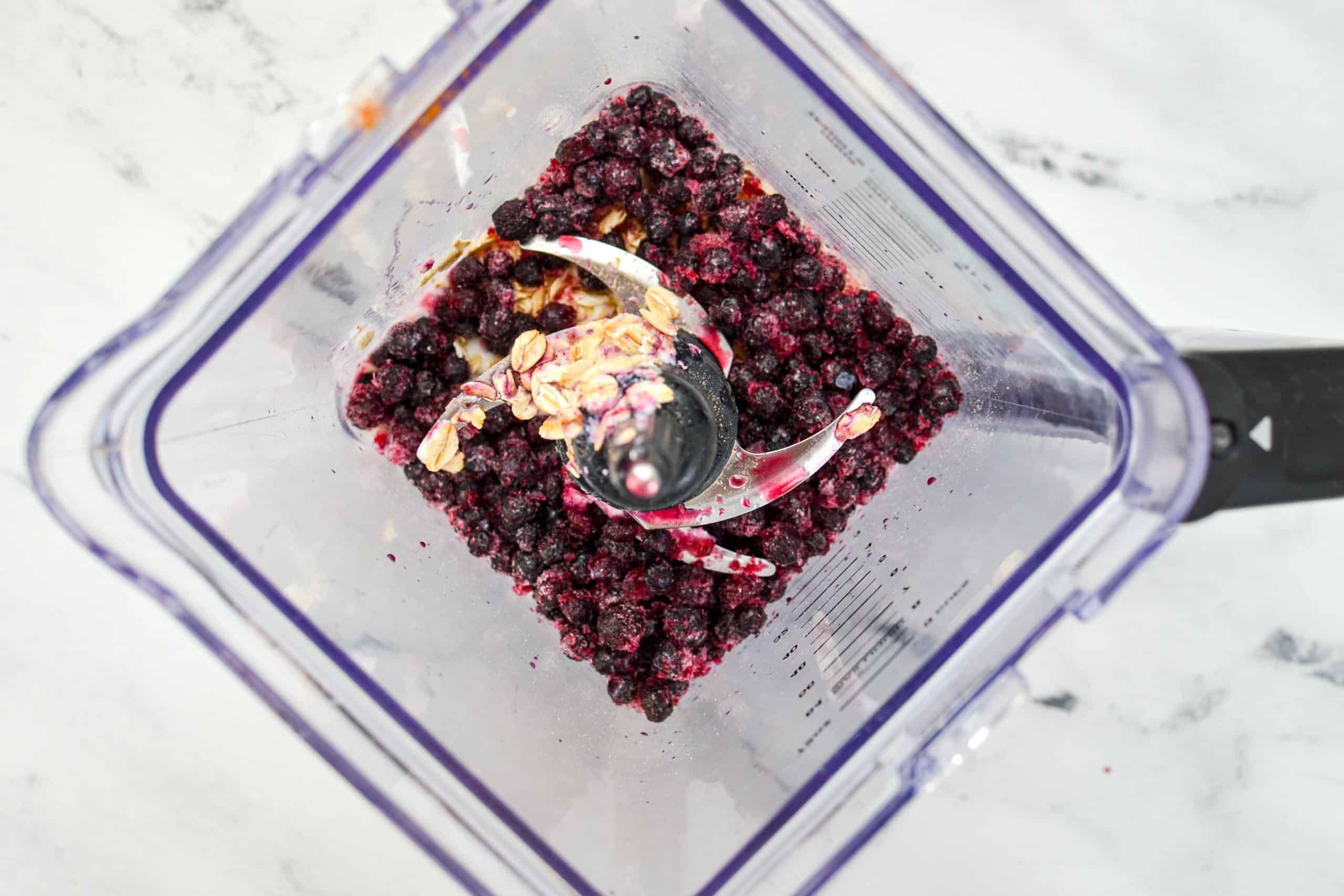 An overhead shot of a blender with frozen blueberries and kefir.