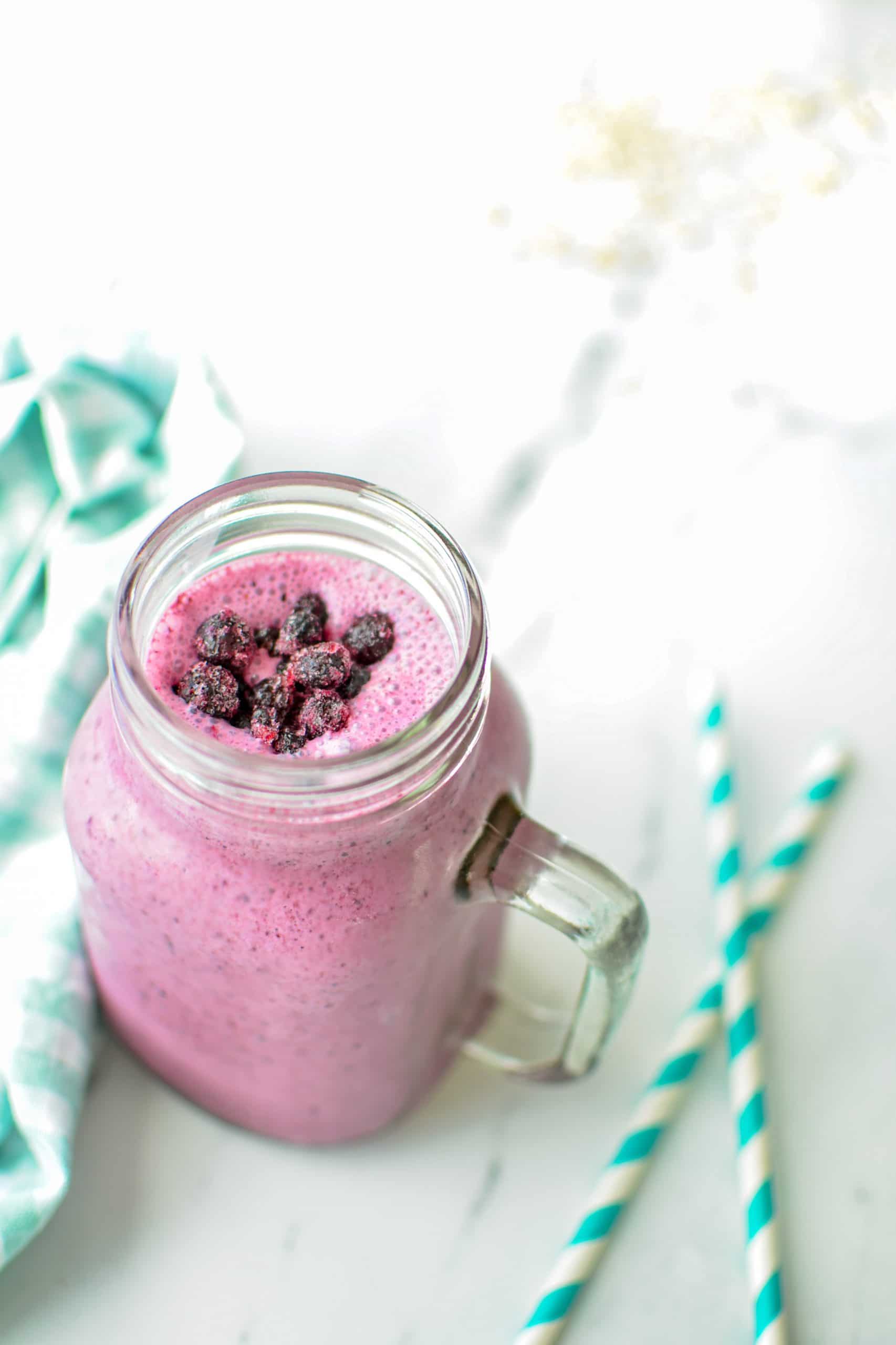 A glass of blueberry smoothie, with two paper straws next to the smoothie.