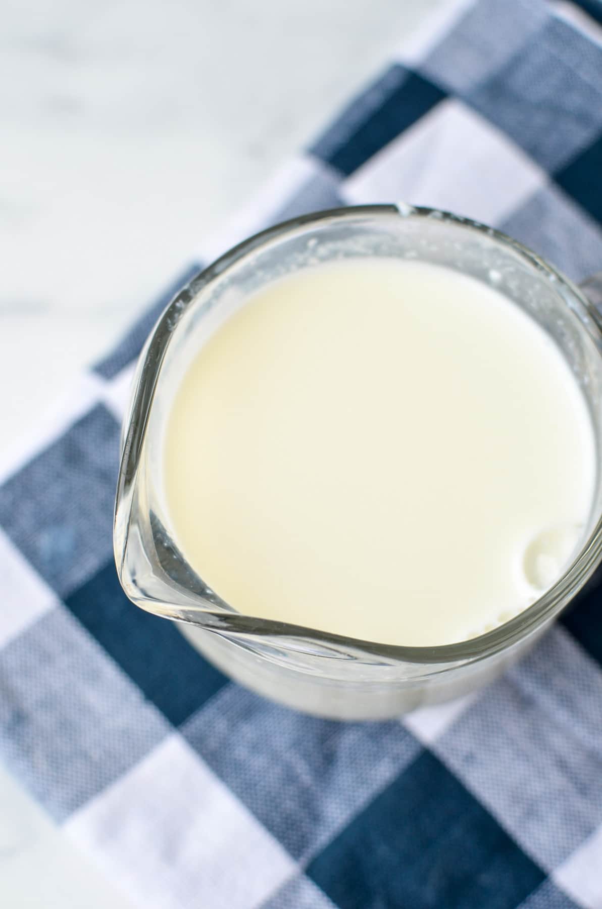 A small pouring glass filled with curdled milk, resting on a blue check napkin.