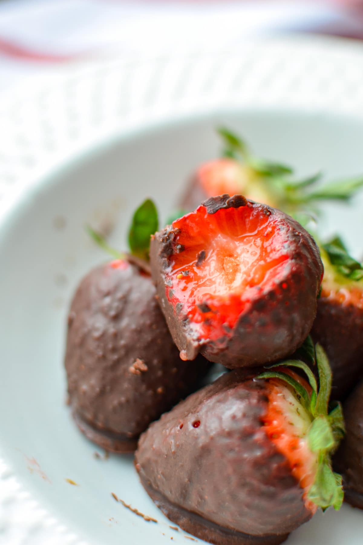 A plate of chocolate covered strawberries with a bite taken out of one.