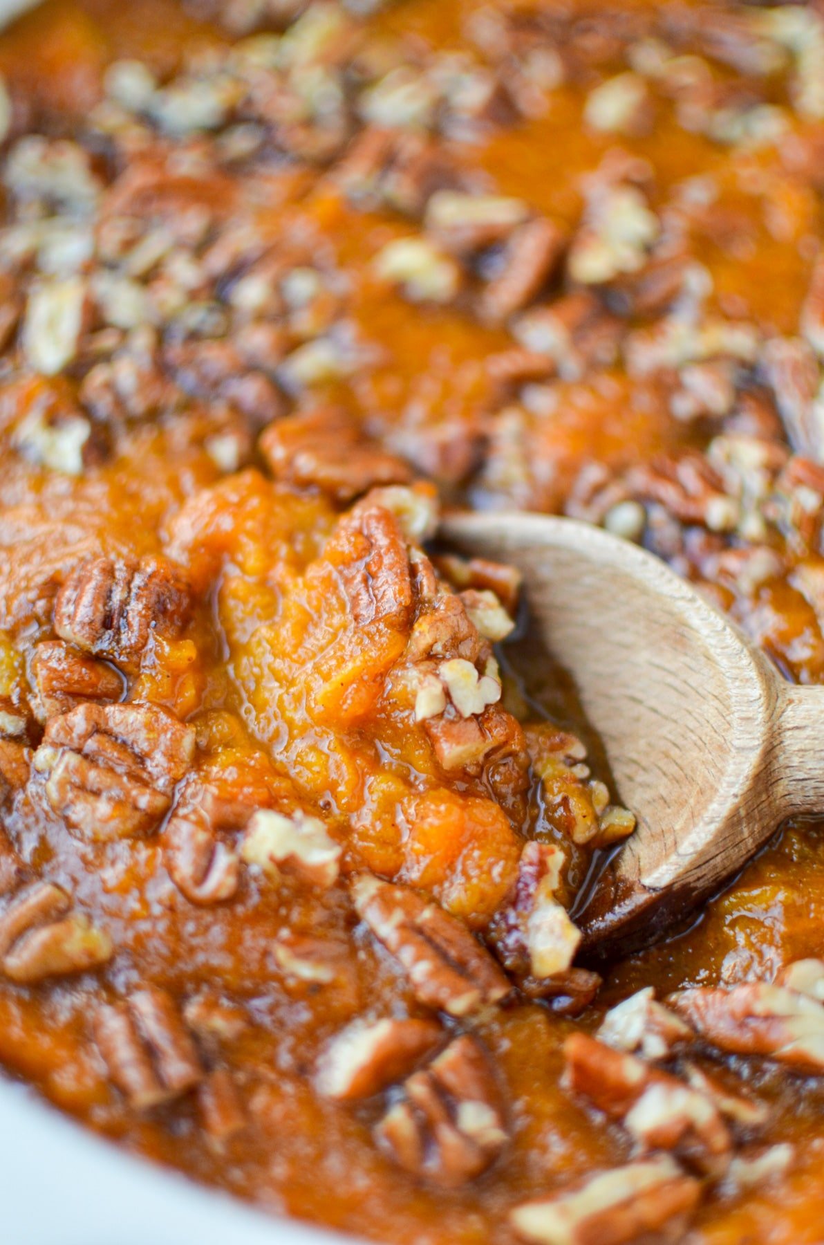 A wooden spoon scooping out a portion of sweet potato casserole with a praline topping.