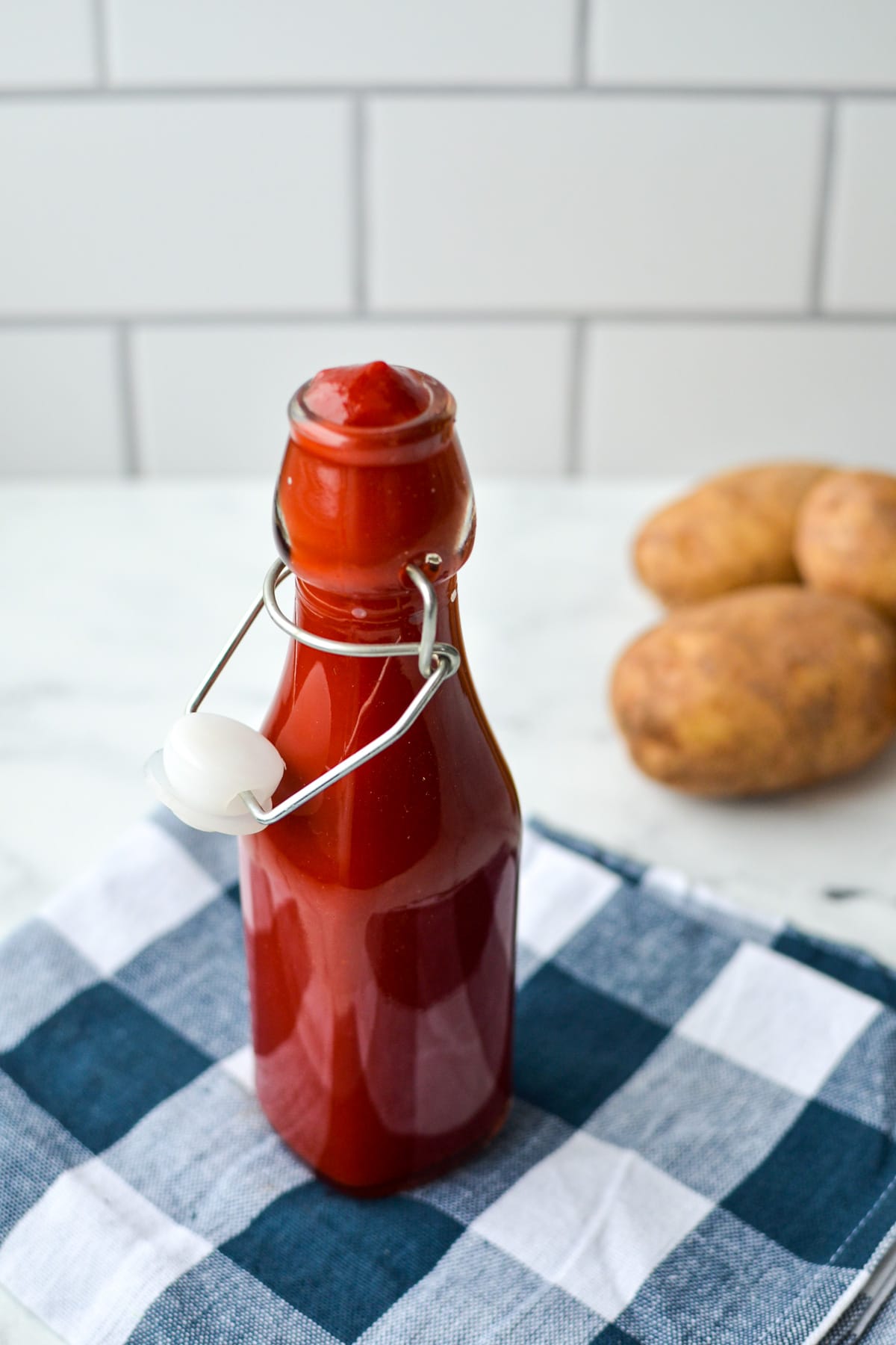 A bottle of homemade ketchup resting on a blue check napkin. 