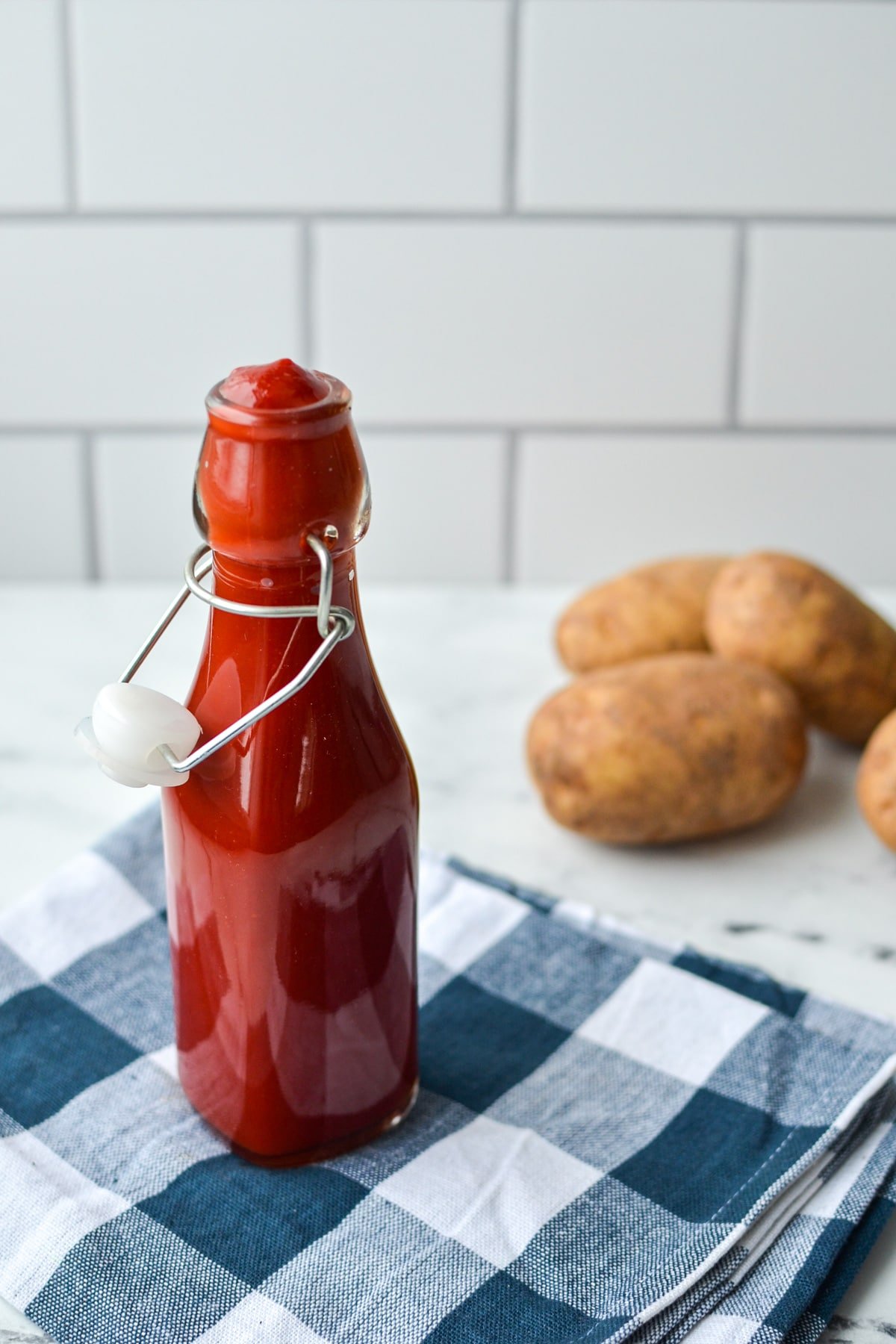 A bottle of homemade ketchup with potatoes in the background.