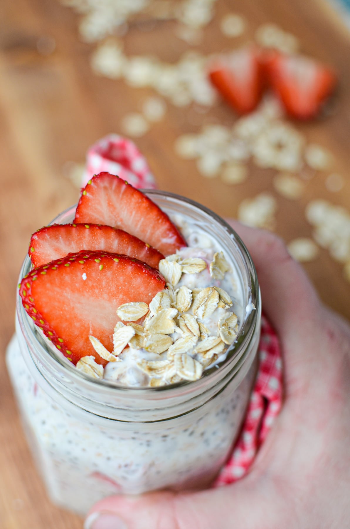 A hand grabbing a jar of kefir overnight oats garnished with strawberries.