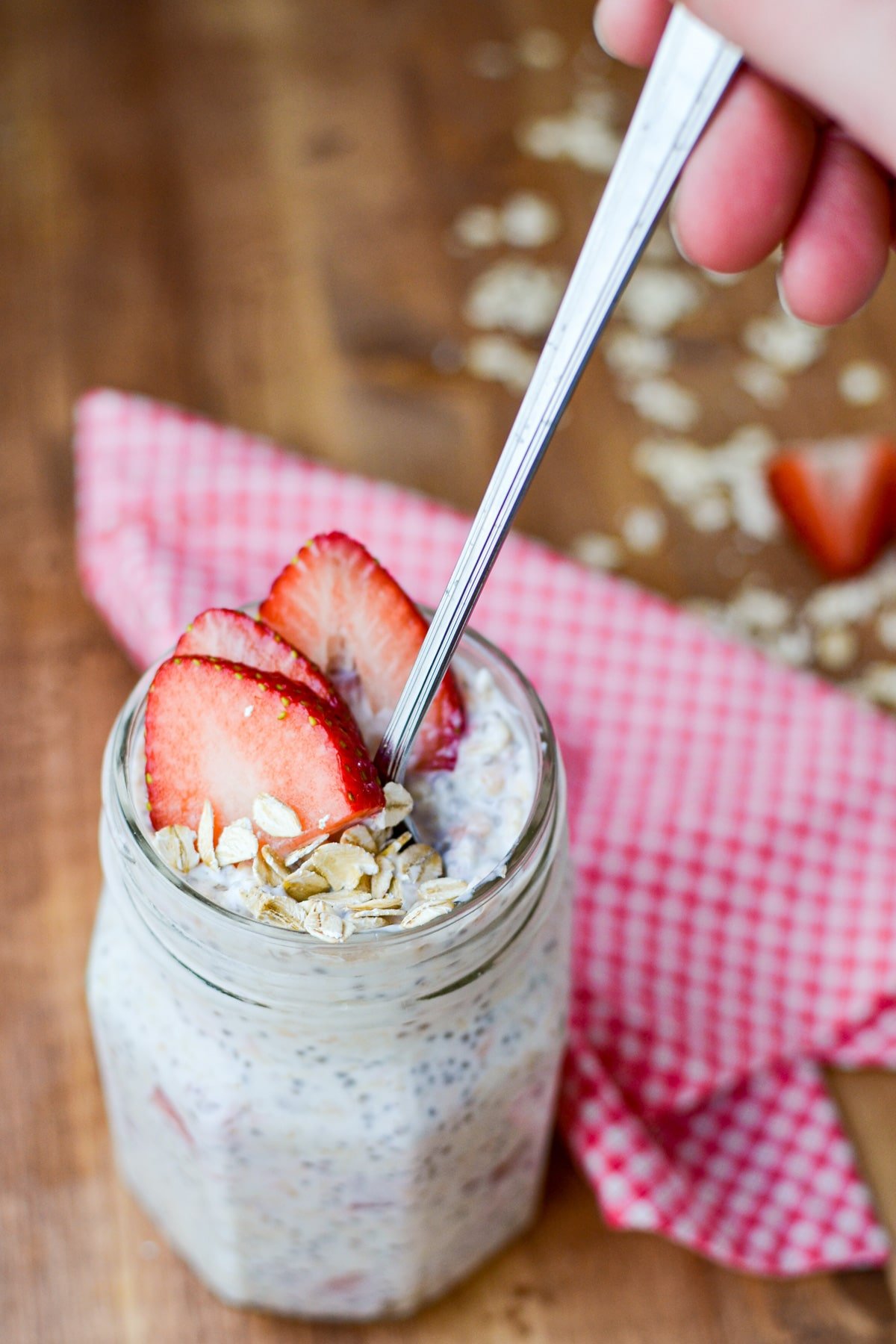 A jar of kefir overnight oats, with someone dipping a spoon into it.