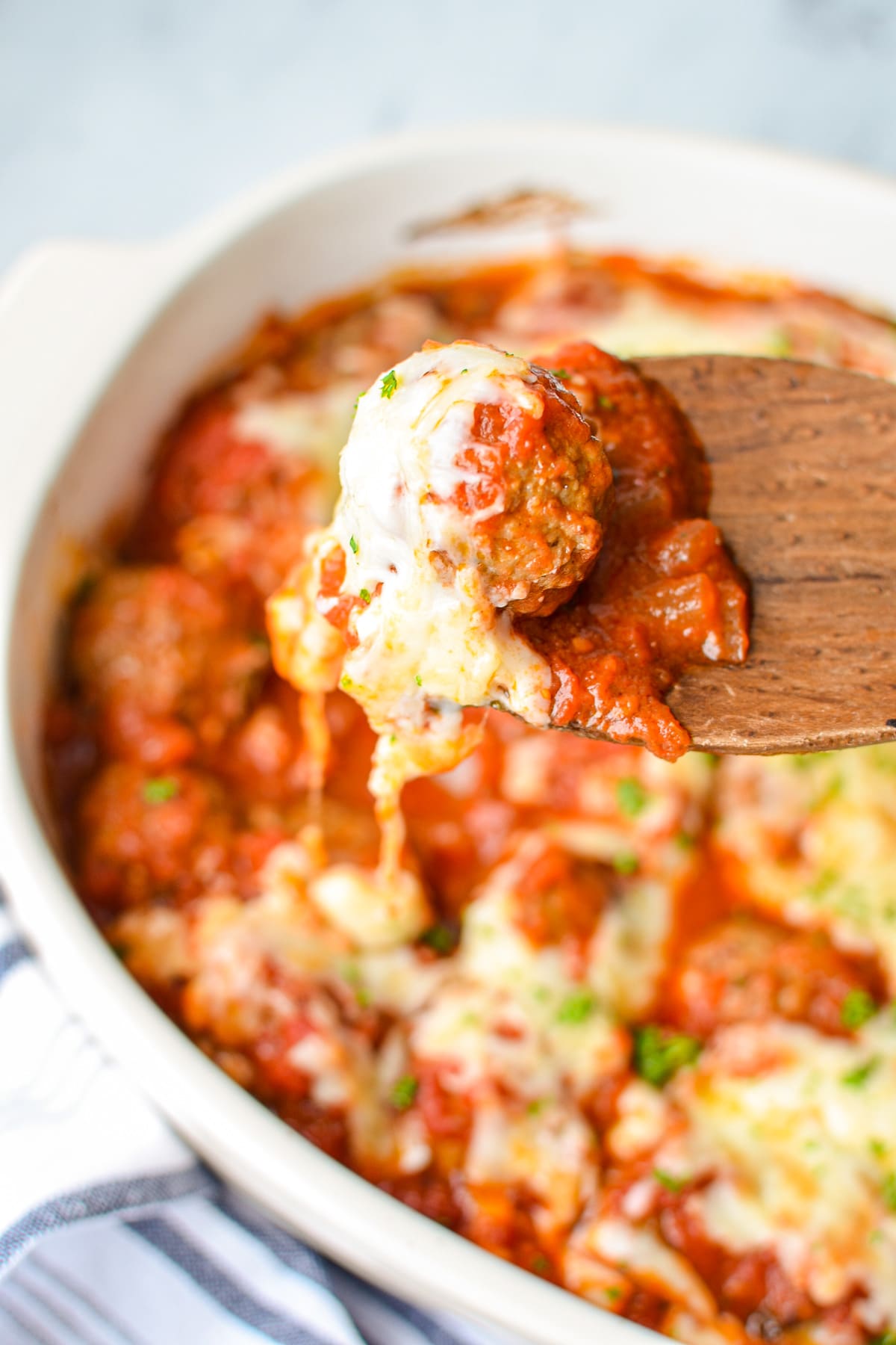 A white baking dish with meatballs and marinara inside. A wooden spoon pulling out a portion 