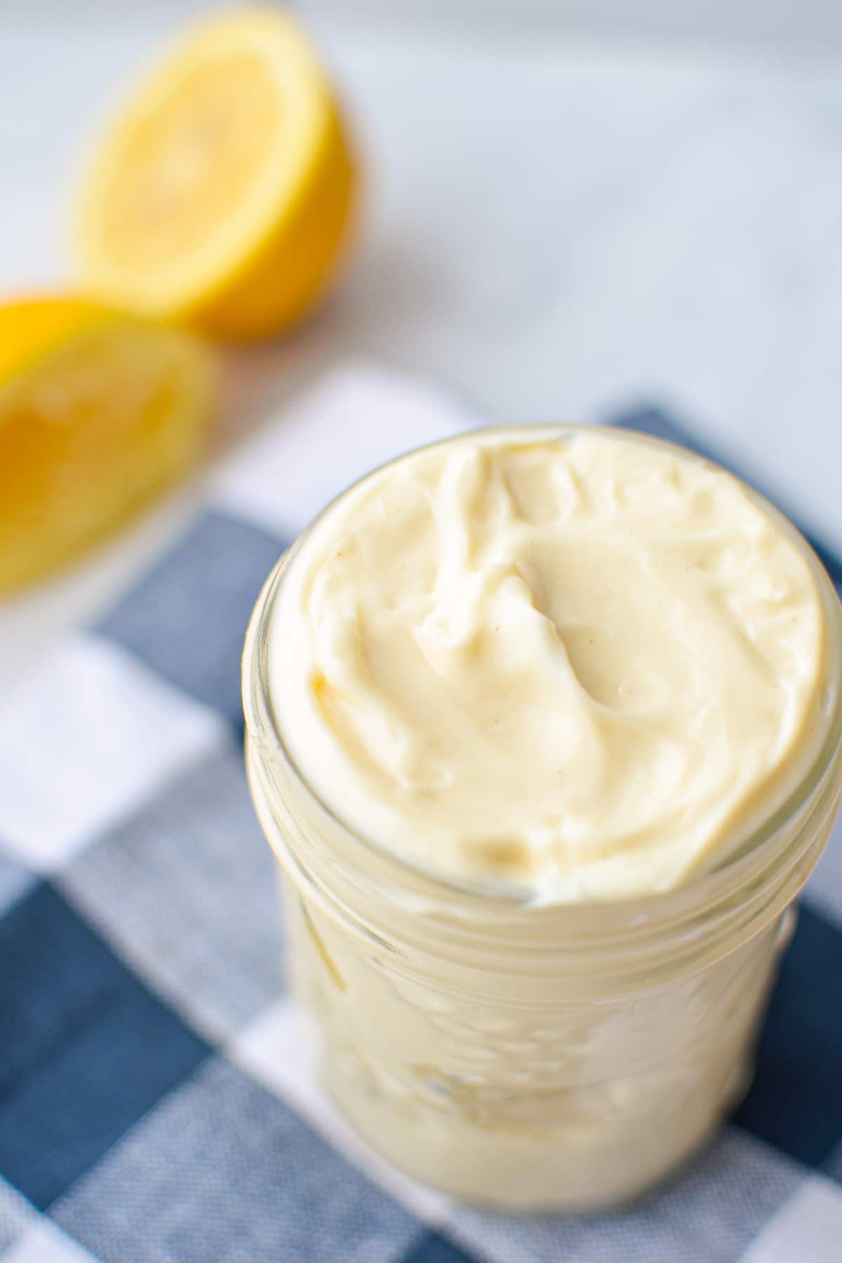 A jar of homemade avocado oil mayo, with a squeezed lemon in the background.