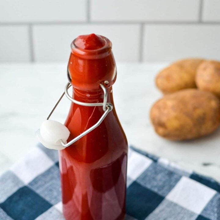 A bottle filled with ketchup and potatoes in the background.
