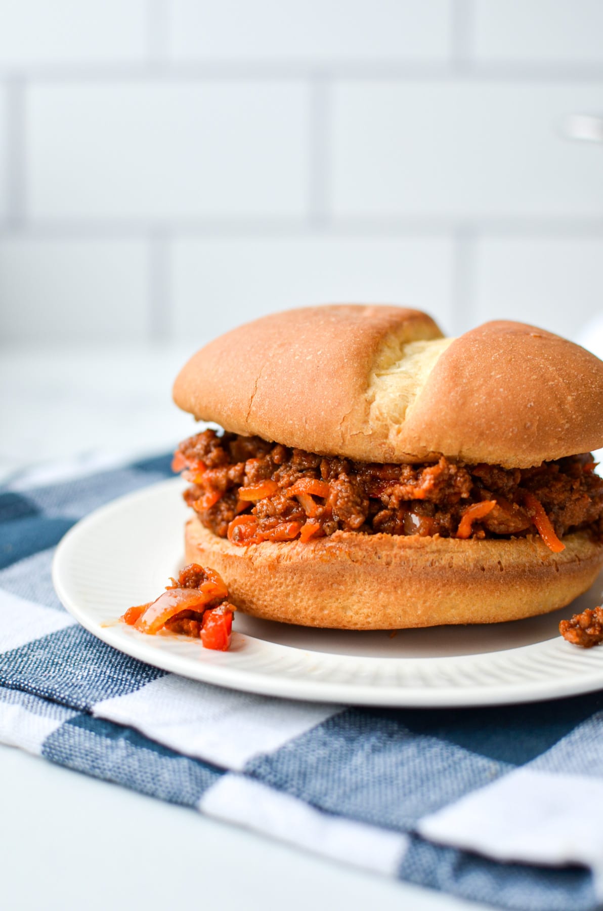 A sloppy joe on a white plate, resting on a blue check napkin.