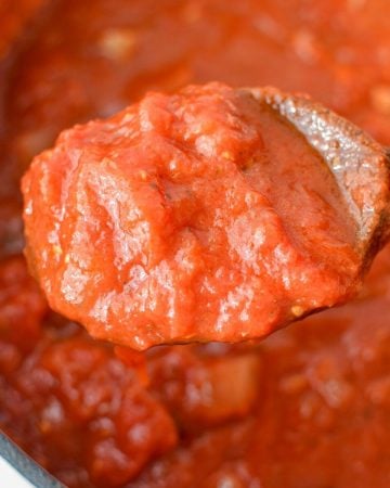 A spoonful of hearty marinara sauce being taken out of a saucepan.
