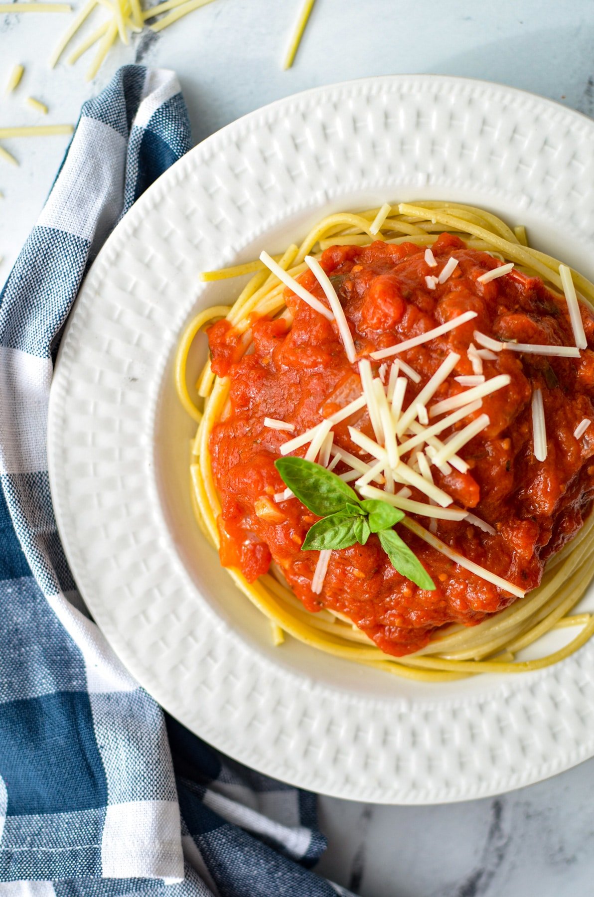 A bowl of spaghetti with marinara sauce, garnished with parmesan cheese and basil.